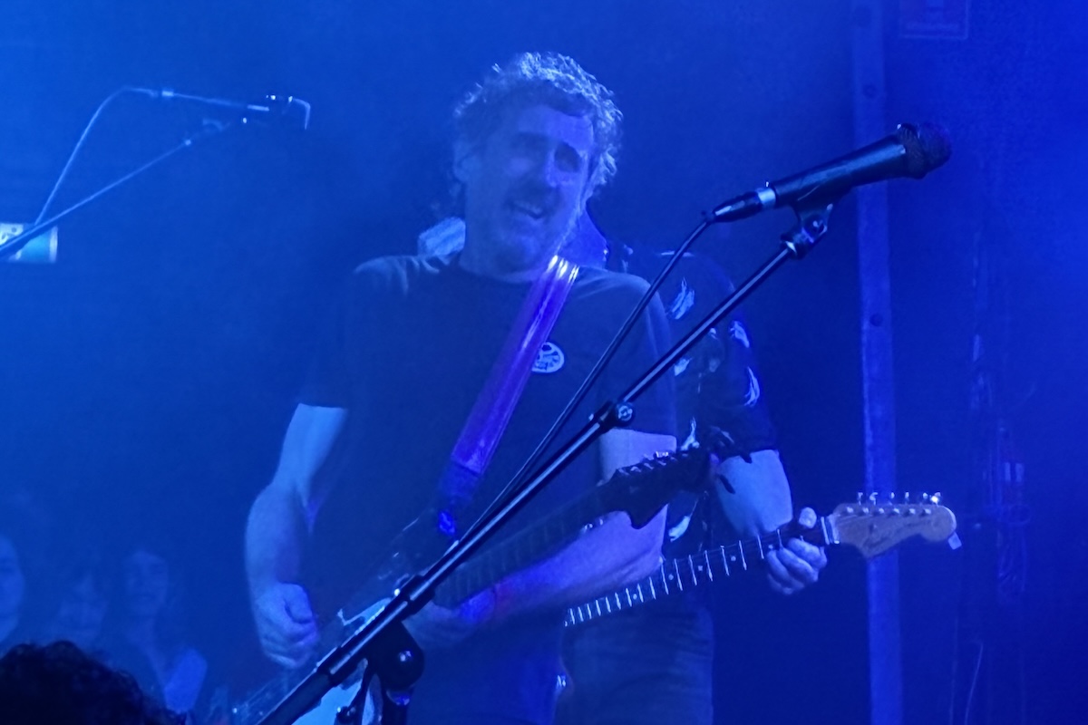 Gareth Liddiard of The Drones playing guitar and singing under blue stage lights at The Gov concert in Adelaide.